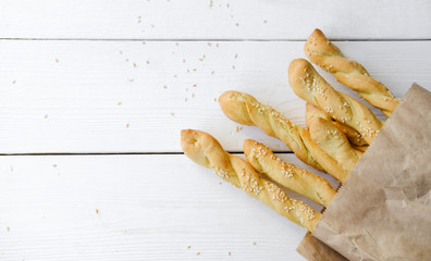 Italian grissini or salted breadsticks. sesame breadsticks in a craft paper on white wooden table. copy space for text. - Powered by Adobe