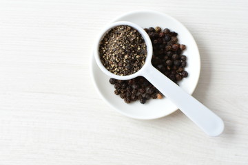 Whole and ground black peppercorns on white wooden background
