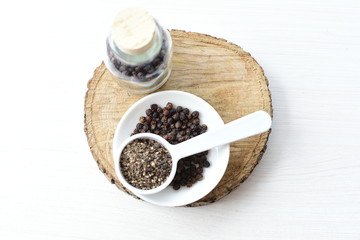 Whole and ground black peppercorns on white wooden background