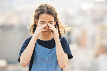 Little girl rubbing her irritated eyes on the city street