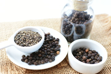 Whole and ground black peppercorns on white wooden background