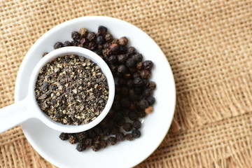 Whole and ground black peppercorns on white wooden background