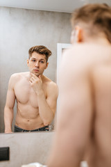 Fototapeta na wymiar gorgeous caucasian muscular man look at reflection on mirror, young man with naked torso look at his shaved beard after bath. hygiene concept