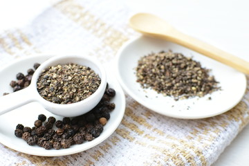 Whole and ground black peppercorns on white wooden background