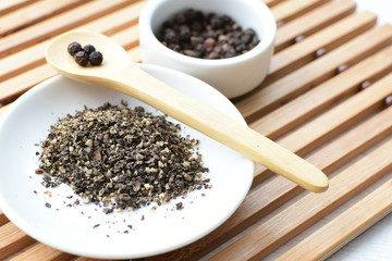 Whole and ground black peppercorns on white wooden background