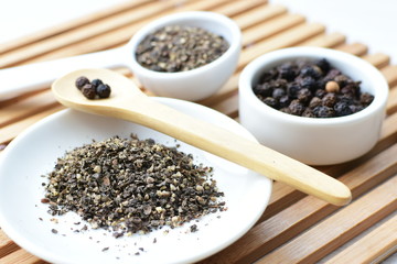 Whole and ground black peppercorns on white wooden background