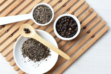 Whole and ground black peppercorns on white wooden background