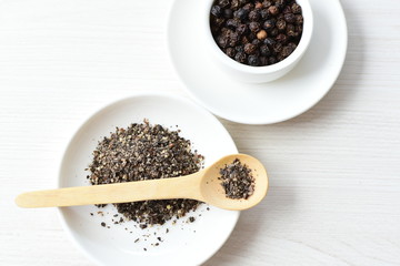 Whole and ground black peppercorns on white wooden background