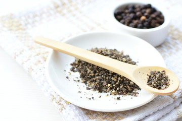 Whole and ground black peppercorns on white wooden background