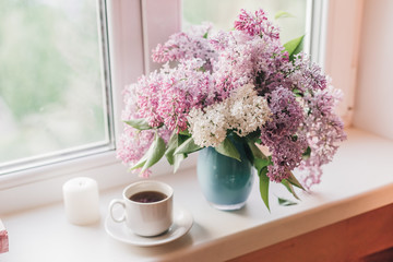 Bouquet of lilacs in a vase and a cup of coffee on the window