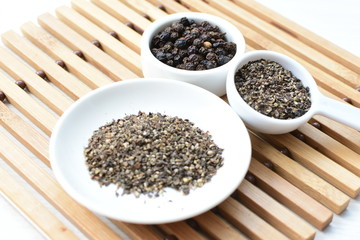 Whole and ground black peppercorns on white wooden background