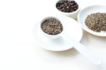 Whole and ground black peppercorns on white wooden background