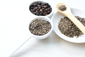 Whole and ground black peppercorns on white wooden background