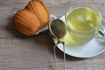 French madeline cakes next to a glass of green tea on a wooden table background