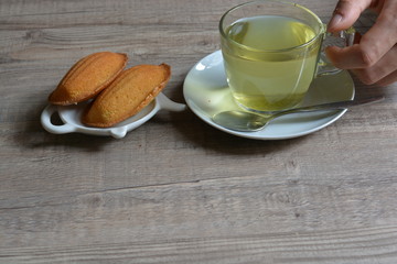 French madeline cakes next to a glass of green tea on a wooden table background