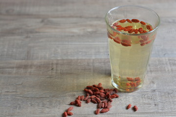 Goji berry drink in a glass with goji berries in it on top of a wooden table