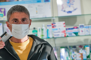 Man wearing face mask in the pharmacy. Coronavirus emergency. Paying by credit card