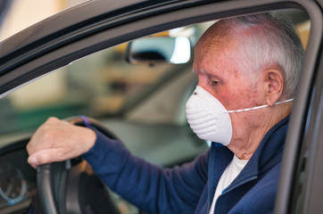 Elderly man wearing face mask entering his car at home