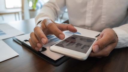 Businessman using smartphone to checking the company performance chart in the office. Business concept.