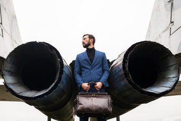 A bearded man with a travel bag near a jet plane.