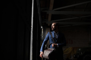 Fototapeta na wymiar A man with a beard in a suit and carrying a travel bag is in a dark room.