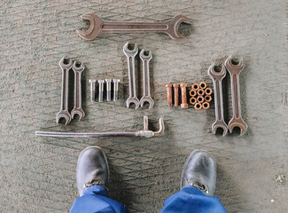 Worker's legs and a set of metal parts for work: wrenches, welded auxiliary keys, rusty and new...