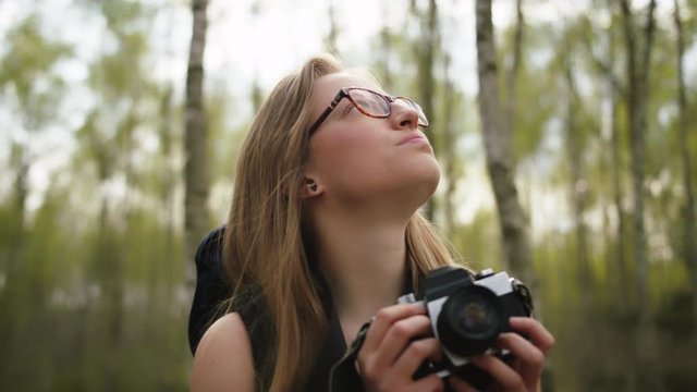 Happy caucasian woman with vintage camera enjoying holiday in the nature. Backpacker in the forest. 