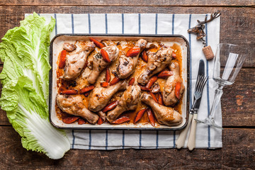 A lot of fried caramel chicken legs on a tray  with vegetables on a authentic wooden table.  Corkscrew, wine glass and vintage cutlery. Mexican, Chinese authentic cuisine.