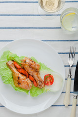 Fried chicken legs in caramelized sauce on a white rustic plate with garnish of baked and fresh vegetables.  Glass of water and wine, vintage cutlery. Mexican, Chinese authentic cuisine. Organic