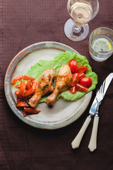 Fried chicken legs in caramelized sauce on a white rustic plate with garnish of baked and fresh vegetables on a brown tablecloth. Mexican, Chinese authentic cuisine. Organic products. View from above.