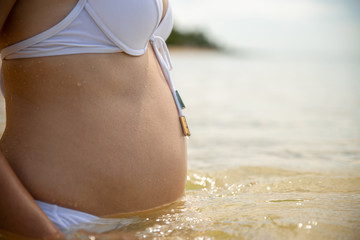 Fototapeta premium pregnant woman in a white bikini separate swimsuit is standing in the sea