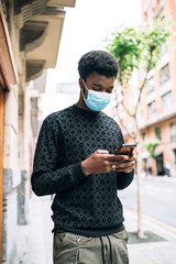 African-American black guy walking down the street with a blue face mask staring at his cell phone