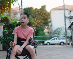 Obraz premium Asian special child on wheelchair is playing badminton to strengthen muscles in the house, Lifestyle of disabled child,Life in the education age of children, Happy disability kid stay at home concept.