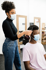 African-American hairdresser combing an African-American man in a mask
