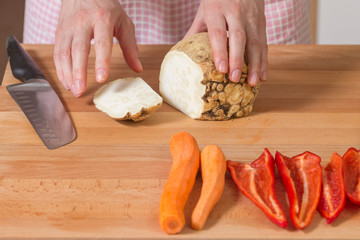 Close up of hands peeling and cutting celery root on a wooden board. Healthy food preparation concept