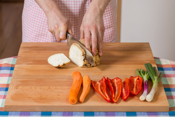 Close up of hands peeling and cutting celery root on a wooden board. Healthy food preparation concept