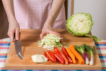 Close up of hands chopping white cabbage on a wooden board. Healthy food preparation concept