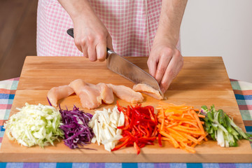 Close up of hands slicing chicken breast on a wooden board. Healthy food preparation concept