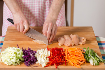 Close up of hands slicing chicken breast on a wooden board. Healthy food preparation concept