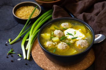 The concept of healthy and diet food. Russian or Ukrainian cuisine. Soup with meatballs, bulgur and pickled cucumbers on a dark stone table.