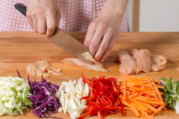 Close up of hands slicing chicken breast on a wooden board. Healthy food preparation concept