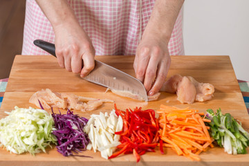 Close up of hands slicing chicken breast on a wooden board. Healthy food preparation concept