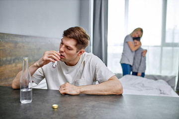 grief in the family when husband is an alcoholic, young caucasian man suffering from alcoholism, unhappy wife and son stand in the background