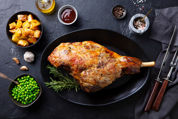 Roasted lamb leg with potato and green peas. Black background. Top view.