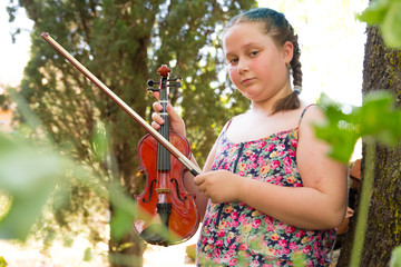 Chubby blonde teenager with braids in her hair playing the violin. Concept children playing instruments in nature.