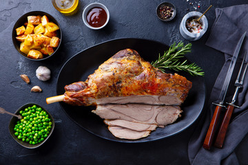 Roasted lamb leg with potato and green peas. Black background. Top view. © annapustynnikova