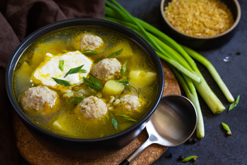 The concept of healthy and diet food. Russian or Ukrainian cuisine. Soup with meatballs, bulgur and pickled cucumbers on a dark stone table.