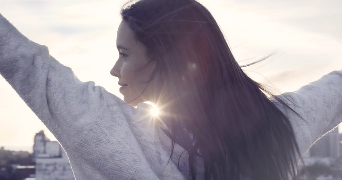 Beautiful woman with open arms at city sunrise smiling. Sky, sun, beauty, freedom.