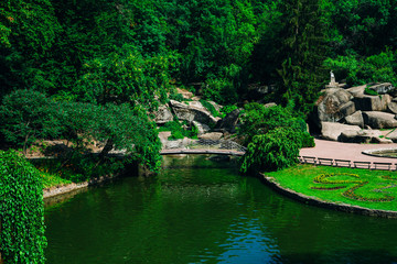 Fototapeta na wymiar Sofia Park, Uman. River in a landscape park on a sunny day. Stone bridge over the river in a green park. Tall trees, river and big stones in the park.