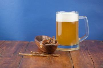 Dried fish in the shape of a straw with beer glass on wooden table. Salted fish delicacies on a table. Close-up.